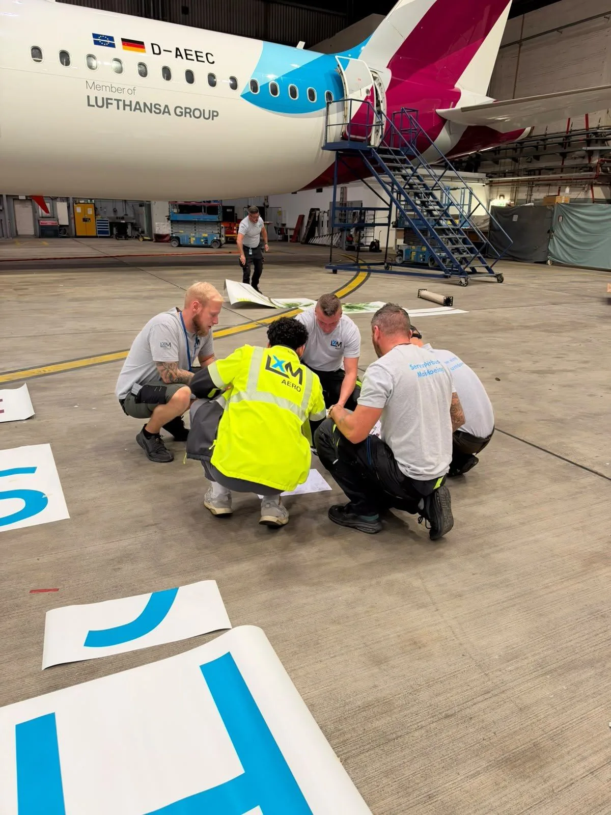 LXM AERO technicians preparing vinyl sections on the hangar floor beside a Eurowings A320